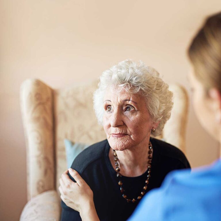 Older adult and caregiver reviewing a daily routine in a bright, supportive living room.
