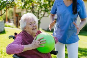 An older adult smiling while watering plants inside a bright, spacious living area.